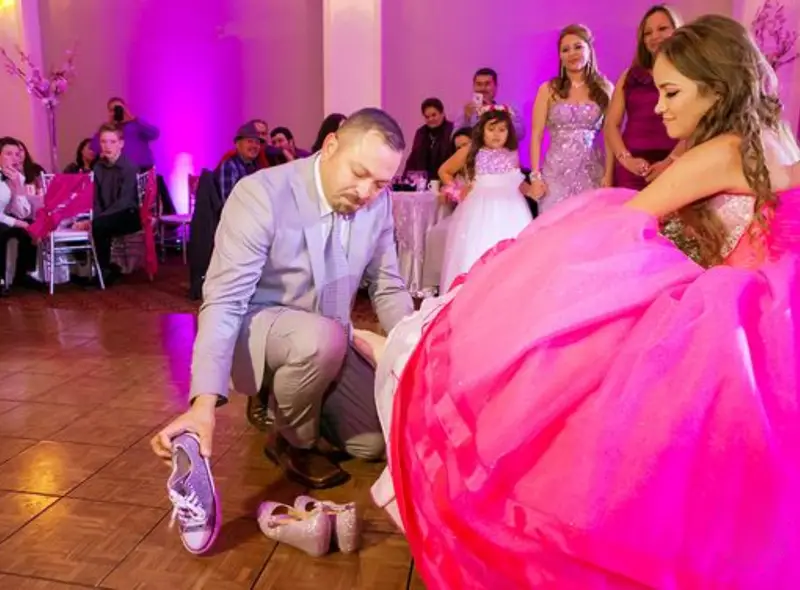 "Padre ayudando a su hija a cambiarse las zapatillas, colocándole los zapatos para su celebración de quinceañera."